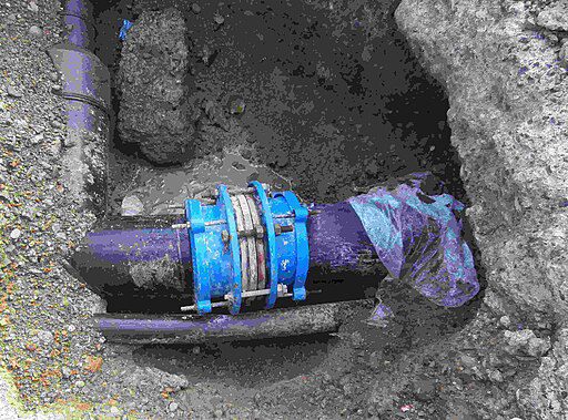 A blue plastic valve and pipe joint installed in a trench with surrounding dirt.