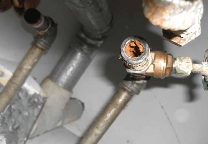 A corroded plumbing valve and open pipe fitting with copper piping in a mechanical space.